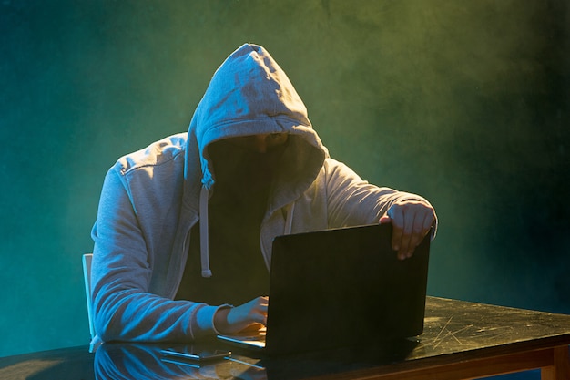 Hooded computer hacker stealing information with laptop Free Photo
